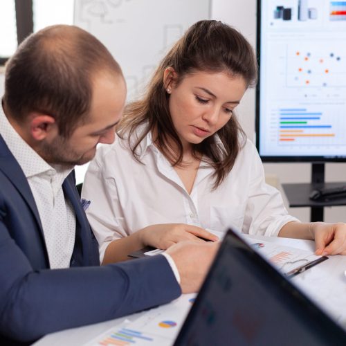 Colleagues of startup business discussing looking at documents in company board brainstorming conference room checking graphs and charts. Financial analysis during briefing.